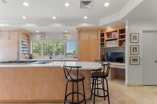 kitchen featuring light brown cabinets, built in desk, a kitchen breakfast bar, stainless steel gas cooktop, and crown molding