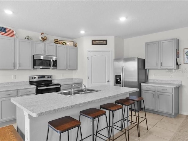 kitchen featuring a breakfast bar area, appliances with stainless steel finishes, light tile patterned floors, and an island with sink