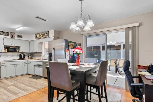 kitchen with backsplash, hanging light fixtures, a notable chandelier, light hardwood / wood-style floors, and stainless steel appliances