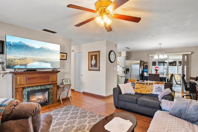 living room with ceiling fan with notable chandelier, light hardwood / wood-style floors, and a high end fireplace