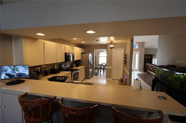 kitchen featuring appliances with stainless steel finishes, light tile patterned floors, kitchen peninsula, and decorative light fixtures