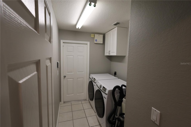 laundry room with independent washer and dryer, light tile patterned flooring, a textured ceiling, and cabinets