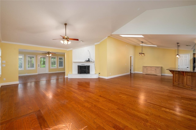 unfurnished living room with a large fireplace, wood-type flooring, ceiling fan with notable chandelier, vaulted ceiling with skylight, and crown molding