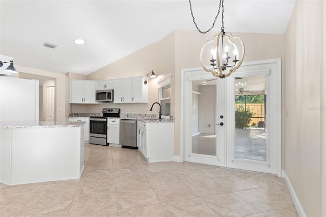 kitchen featuring appliances with stainless steel finishes, lofted ceiling, pendant lighting, white cabinets, and light stone counters