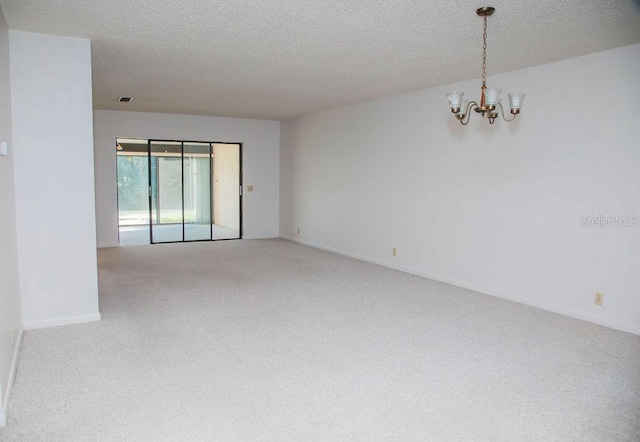 unfurnished room featuring a notable chandelier, carpet flooring, and a textured ceiling