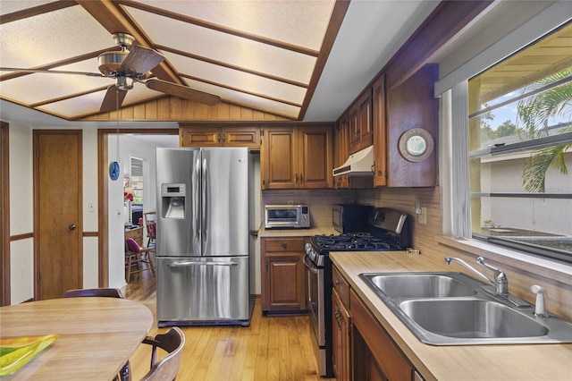 kitchen featuring tasteful backsplash, appliances with stainless steel finishes, vaulted ceiling, light hardwood / wood-style flooring, and sink