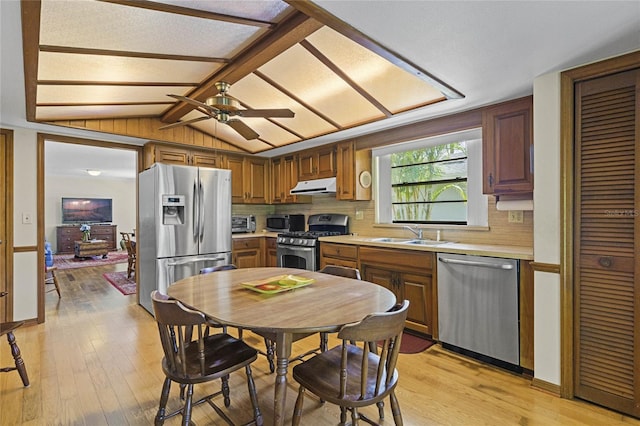 kitchen featuring ceiling fan, light wood-type flooring, sink, wooden walls, and stainless steel appliances