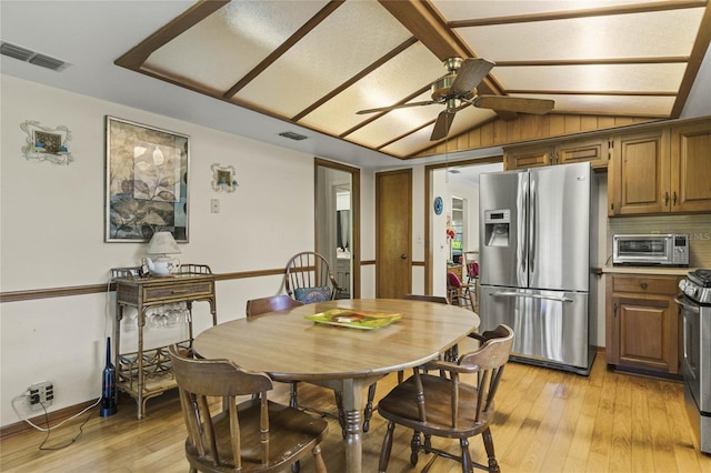 dining room with ceiling fan, lofted ceiling, light wood-type flooring, and wooden walls