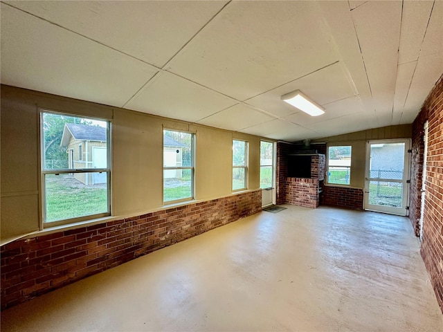 interior space with concrete floors, lofted ceiling, a healthy amount of sunlight, and brick wall