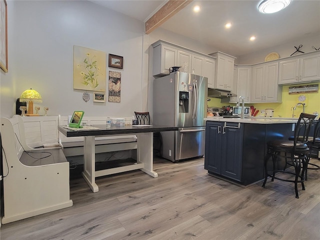 kitchen featuring gray cabinetry, light hardwood / wood-style floors, stainless steel fridge, and a kitchen bar