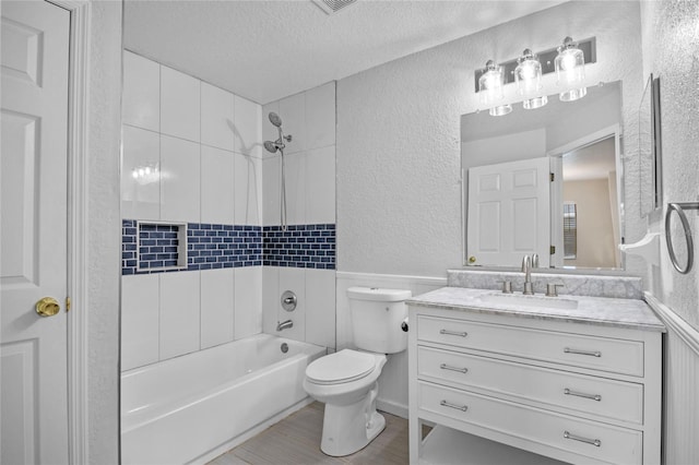 full bathroom with wood-type flooring, tiled shower / bath combo, vanity, toilet, and a textured ceiling