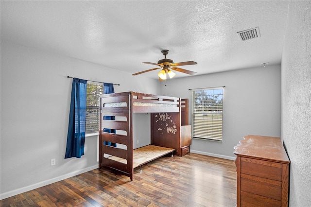 bedroom with multiple windows, ceiling fan, dark hardwood / wood-style floors, and a textured ceiling