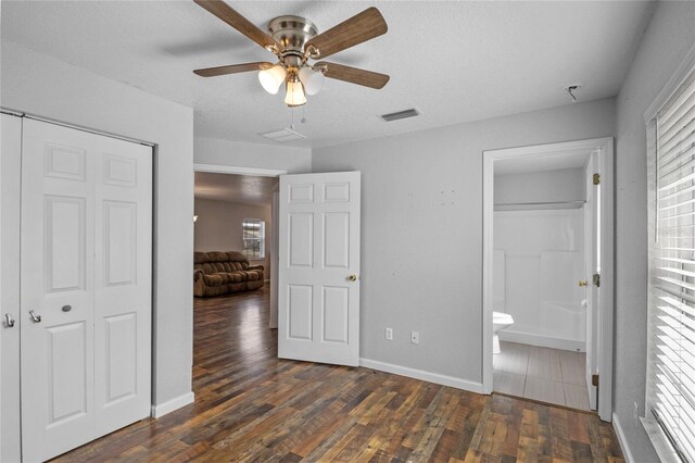 unfurnished bedroom featuring multiple windows, ceiling fan, connected bathroom, and dark hardwood / wood-style flooring