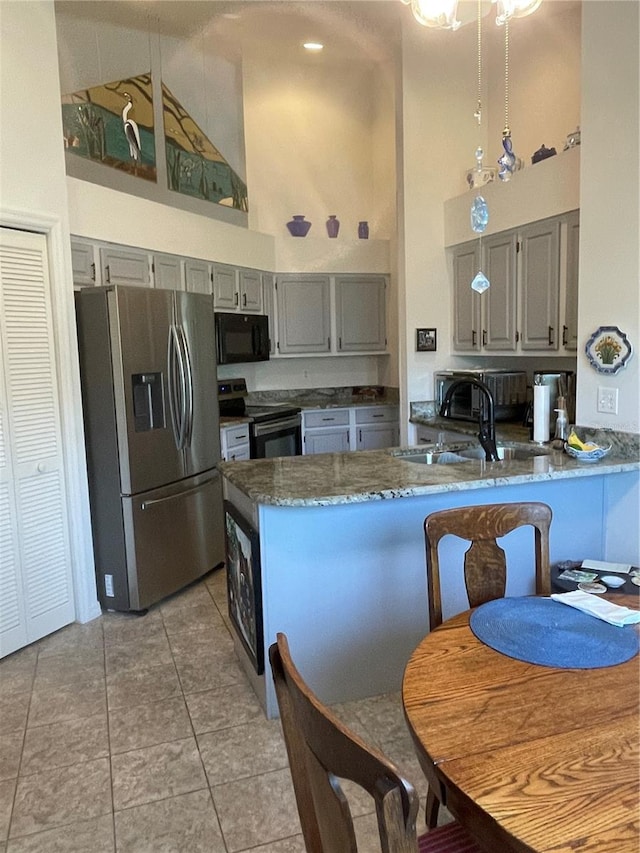 kitchen with kitchen peninsula, appliances with stainless steel finishes, high vaulted ceiling, light tile patterned flooring, and sink