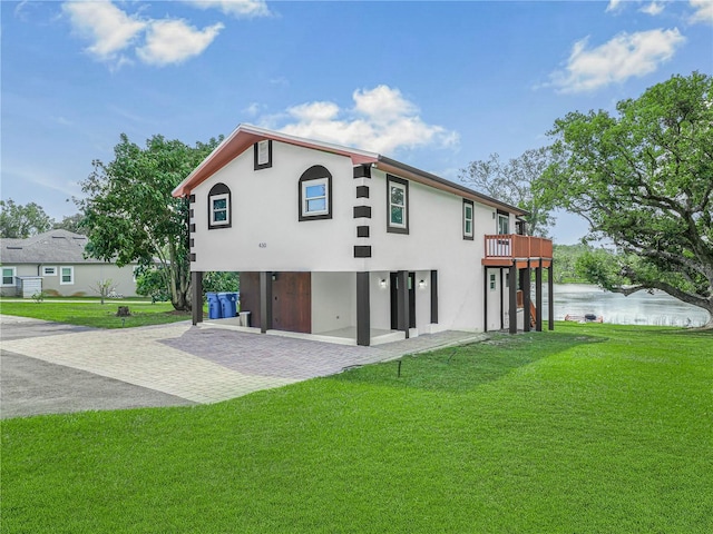 rear view of house featuring a patio, a lawn, a water view, and stucco siding