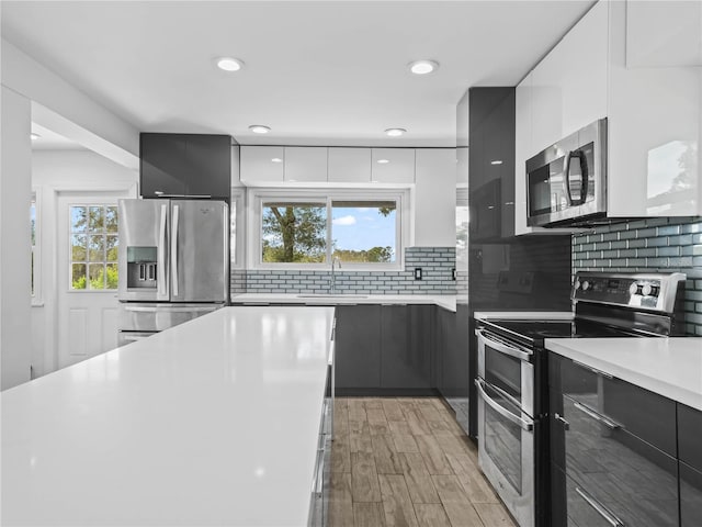 kitchen featuring stainless steel appliances, light countertops, light wood-style floors, modern cabinets, and tasteful backsplash