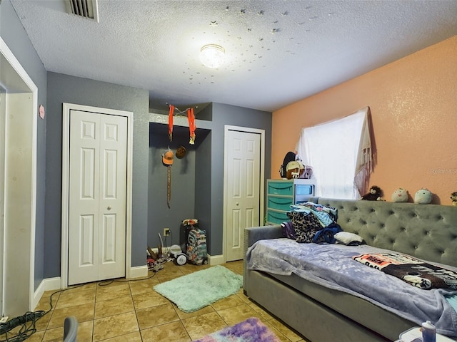 bedroom with a textured ceiling, light tile patterned floors, and two closets