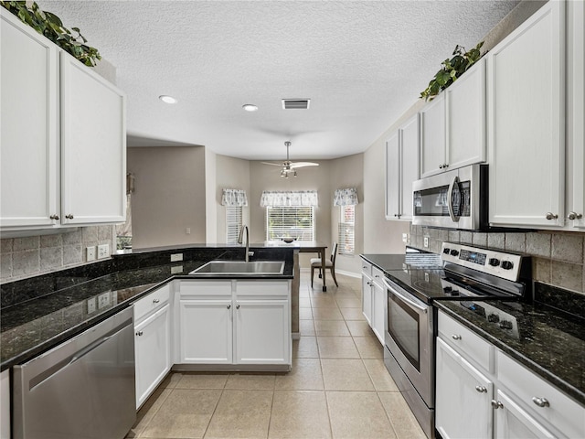 kitchen featuring stainless steel appliances, white cabinetry, sink, dark stone counters, and light tile patterned floors