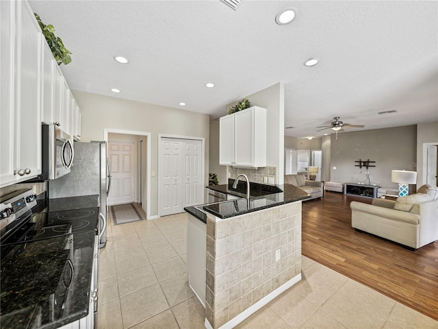 kitchen featuring dark stone counters, kitchen peninsula, electric range, white cabinetry, and light wood-type flooring