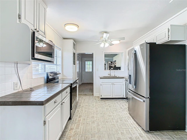 kitchen with tile counters, stainless steel appliances, sink, light wood-type flooring, and white cabinetry