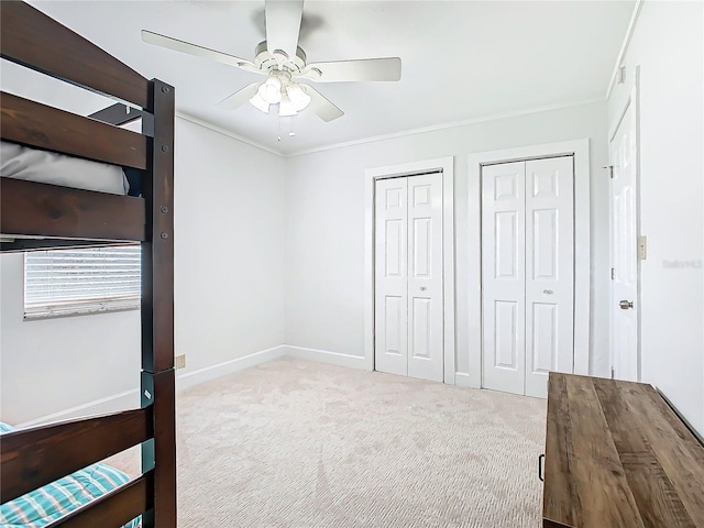 unfurnished bedroom with light carpet, crown molding, two closets, and ceiling fan