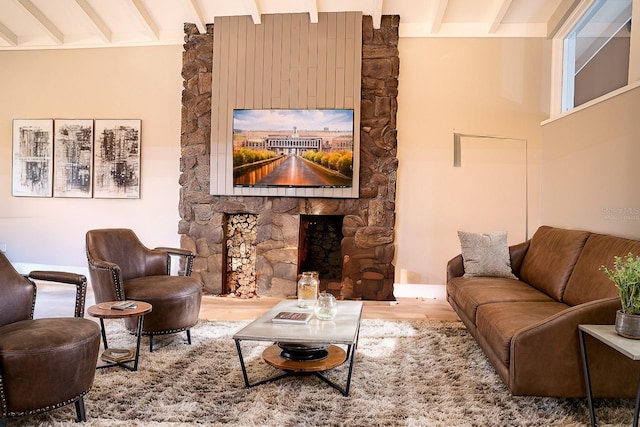 living room with beamed ceiling, a stone fireplace, and wood-type flooring