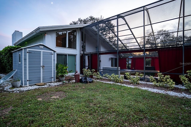 rear view of house featuring glass enclosure, a storage shed, and a lawn