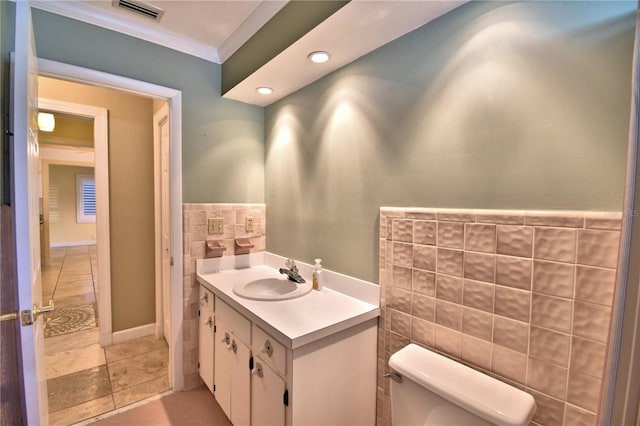 bathroom with toilet, tile walls, ornamental molding, vanity, and tile patterned flooring