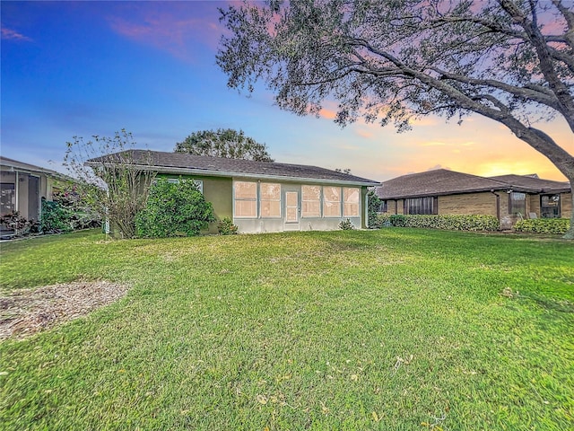 back house at dusk featuring a lawn