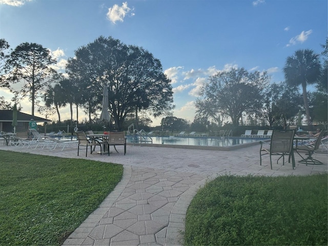 view of home's community with a water view, a yard, a swimming pool, and a patio area