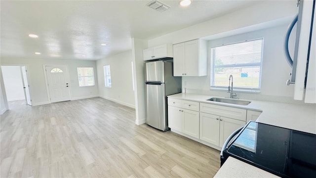 kitchen with white cabinetry, stainless steel refrigerator, sink, and a wealth of natural light