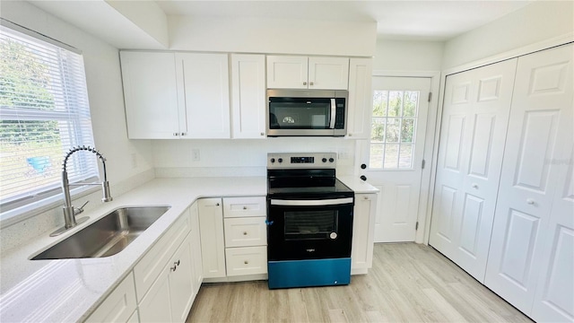 kitchen with light hardwood / wood-style flooring, sink, white cabinetry, appliances with stainless steel finishes, and light stone counters