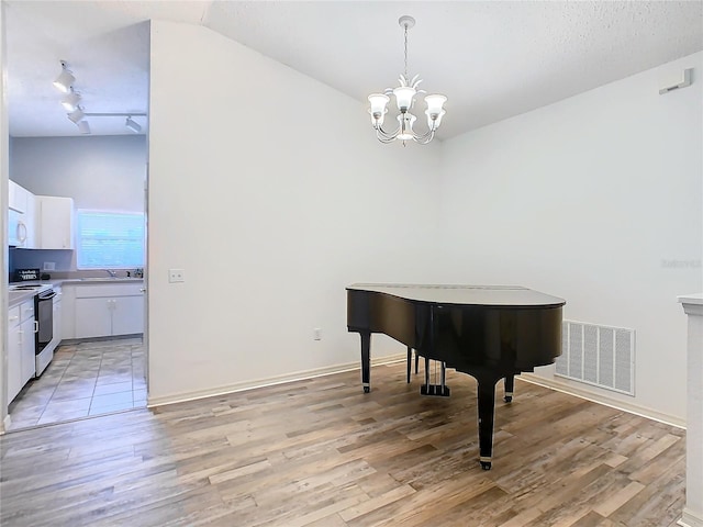 living area with light hardwood / wood-style floors, lofted ceiling, track lighting, and a notable chandelier