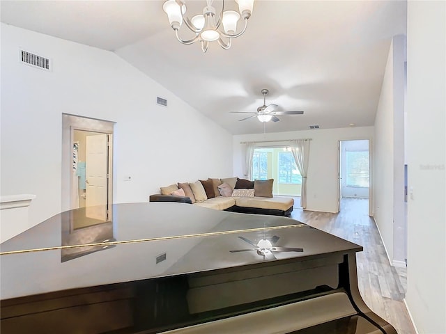 living room featuring ceiling fan with notable chandelier, light hardwood / wood-style floors, and vaulted ceiling