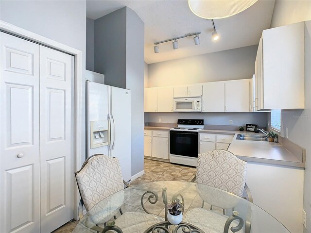 kitchen with sink, white appliances, white cabinets, and a towering ceiling