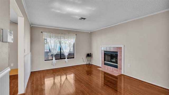 unfurnished living room featuring crown molding, a textured ceiling, a tile fireplace, and hardwood / wood-style floors