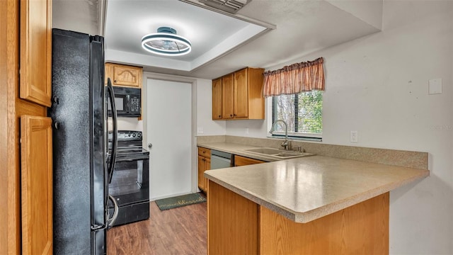 kitchen with kitchen peninsula, a tray ceiling, sink, black appliances, and dark hardwood / wood-style flooring