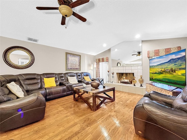 living room featuring a tile fireplace, vaulted ceiling, a textured ceiling, and light wood-type flooring