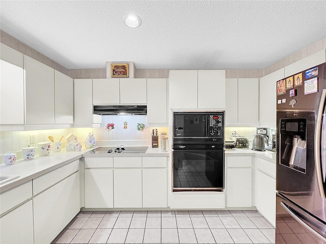 kitchen with light tile patterned floors, a textured ceiling, under cabinet range hood, light countertops, and black appliances