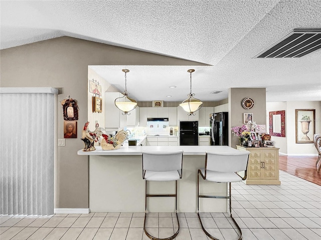 kitchen featuring a peninsula, under cabinet range hood, light countertops, black appliances, and light tile patterned flooring