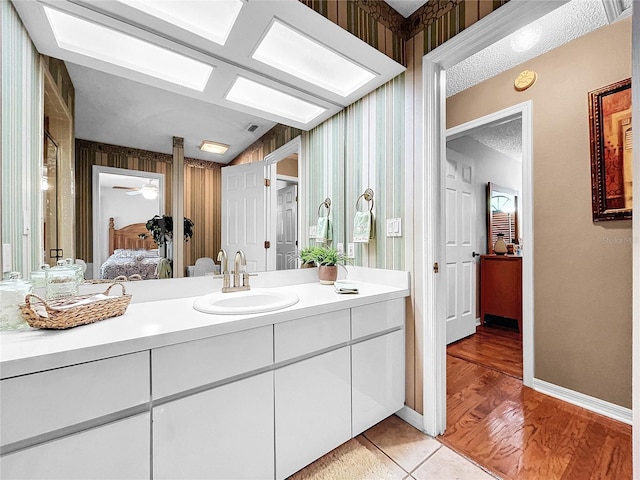 bathroom featuring a textured ceiling, wood finished floors, vanity, baseboards, and ensuite bath