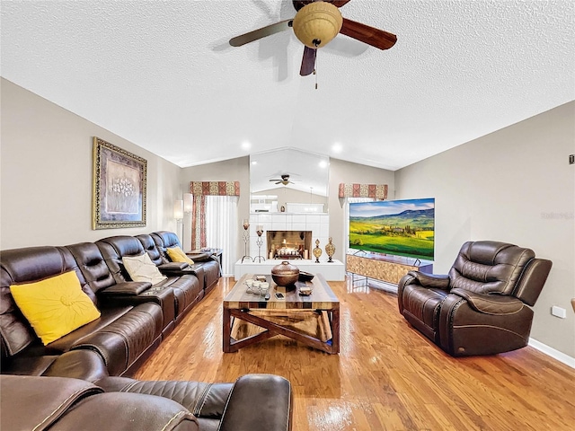 living room featuring lofted ceiling, a textured ceiling, a tile fireplace, a ceiling fan, and light wood-style floors