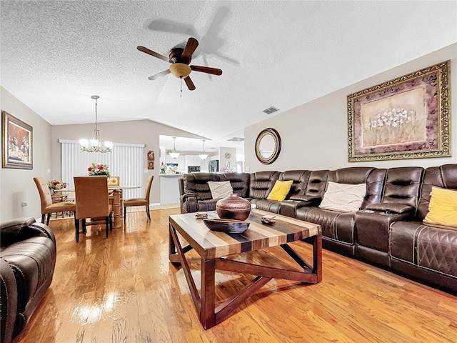 living room featuring visible vents, light wood-style floors, vaulted ceiling, a textured ceiling, and ceiling fan with notable chandelier