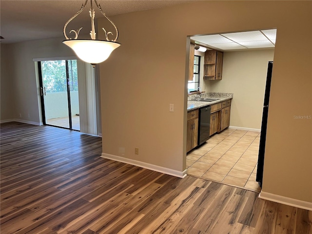 kitchen featuring black dishwasher, light stone countertops, light wood-type flooring, pendant lighting, and sink