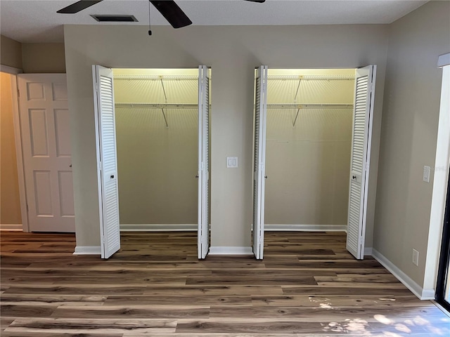 unfurnished bedroom with a textured ceiling, two closets, dark hardwood / wood-style floors, and ceiling fan