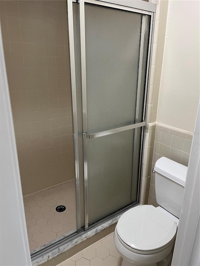 bathroom featuring tile walls, tile patterned floors, toilet, and an enclosed shower