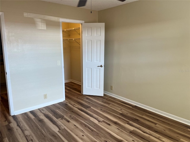 unfurnished bedroom featuring a closet, ceiling fan, dark hardwood / wood-style flooring, and a walk in closet