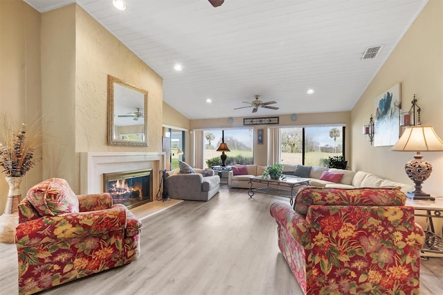 living room with a premium fireplace, vaulted ceiling, ceiling fan, and light hardwood / wood-style flooring