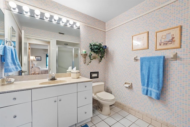 bathroom featuring toilet, a shower with shower door, tile walls, vanity, and tile patterned flooring