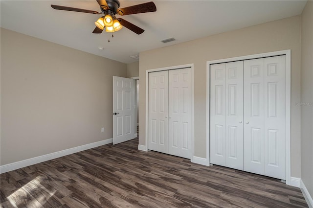 unfurnished bedroom featuring multiple closets, ceiling fan, and dark hardwood / wood-style floors